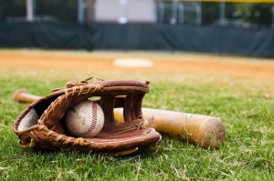 Old baseball, glove, and bat on field with base and outfield in background.