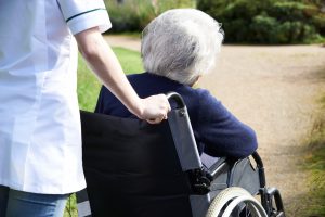 Close Up Of Carer Pushing Senior Woman In Wheelchair